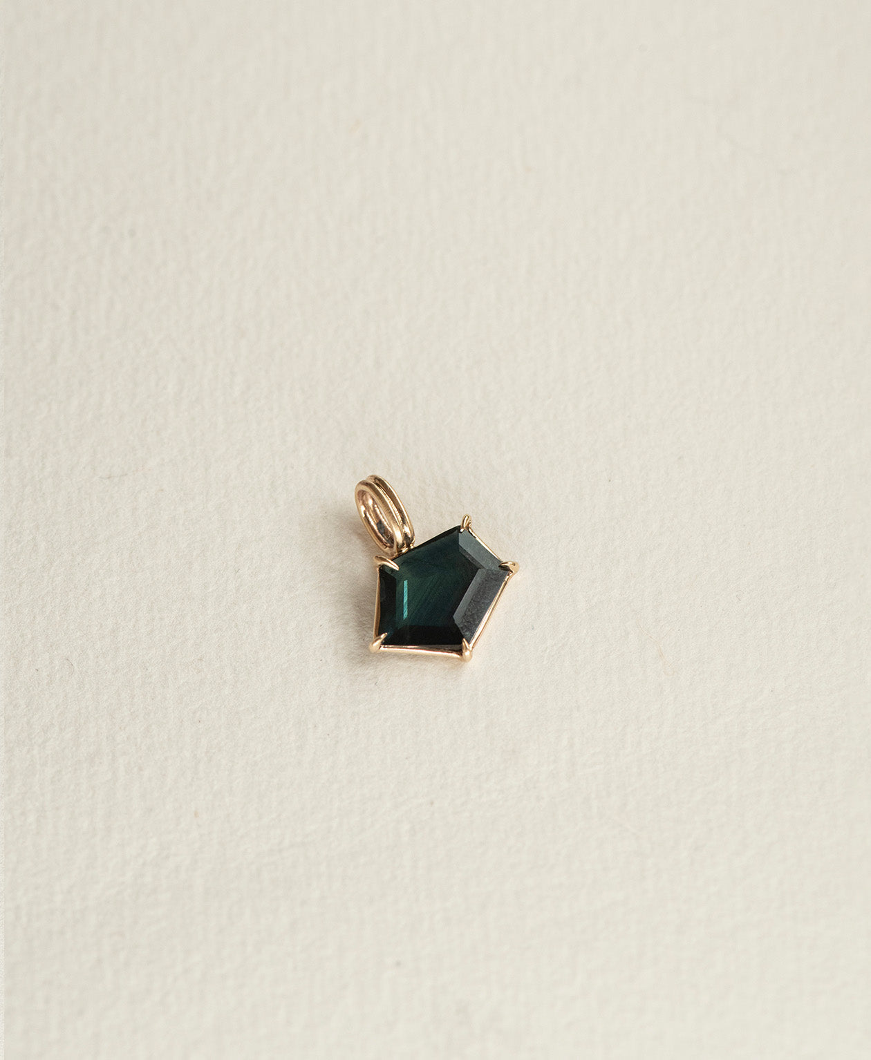 Angled view of the One of a Kind Charm 497 in 9k Yellow Gold with a dark teal portrait cut Sapphire.