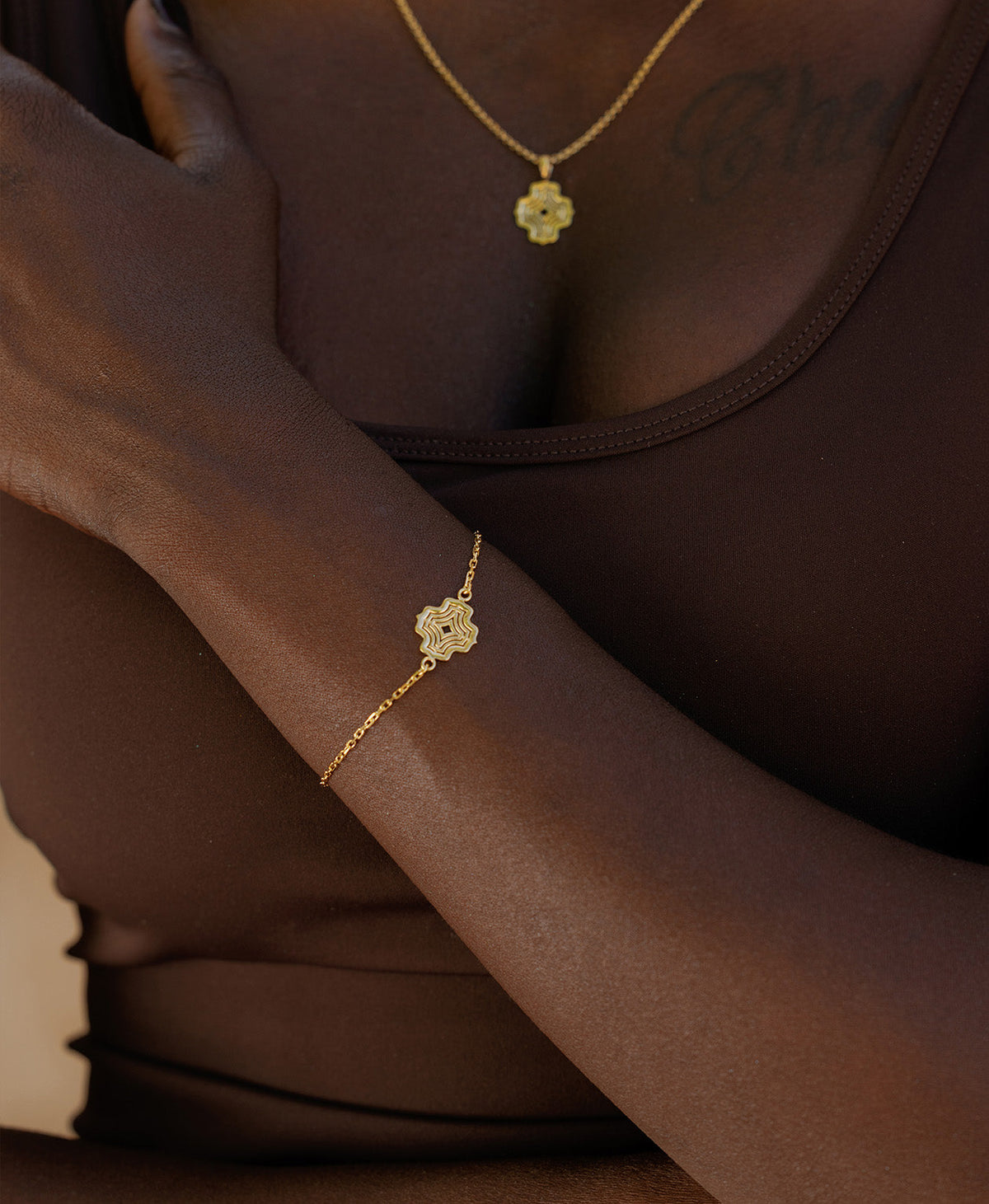 A close-up of a wrist wearing the Alma Bracelet, a gold pendant with a concentric wave design set on a fine cable chain.