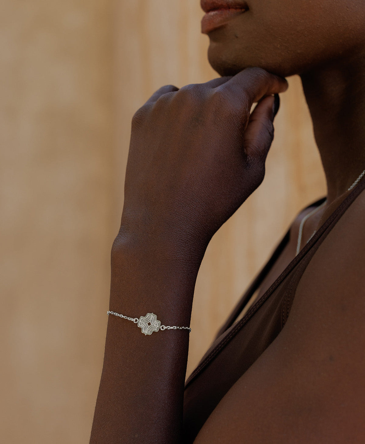 A close-up of an arm wearing the Alma Bracelet, a silver pendant with a concentric wave design set on a fine cable chain.