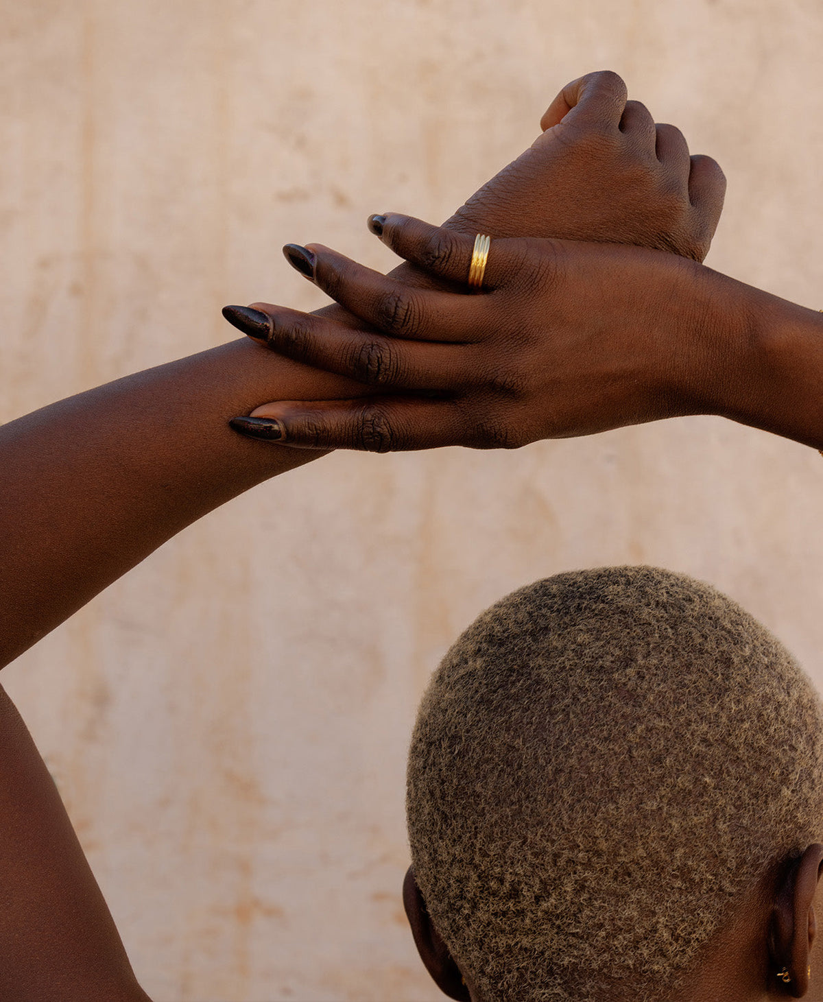 A closeup of a hand and arm, wearing the gold Irma Stacker Ring, formed from three connected bands, layered closely.