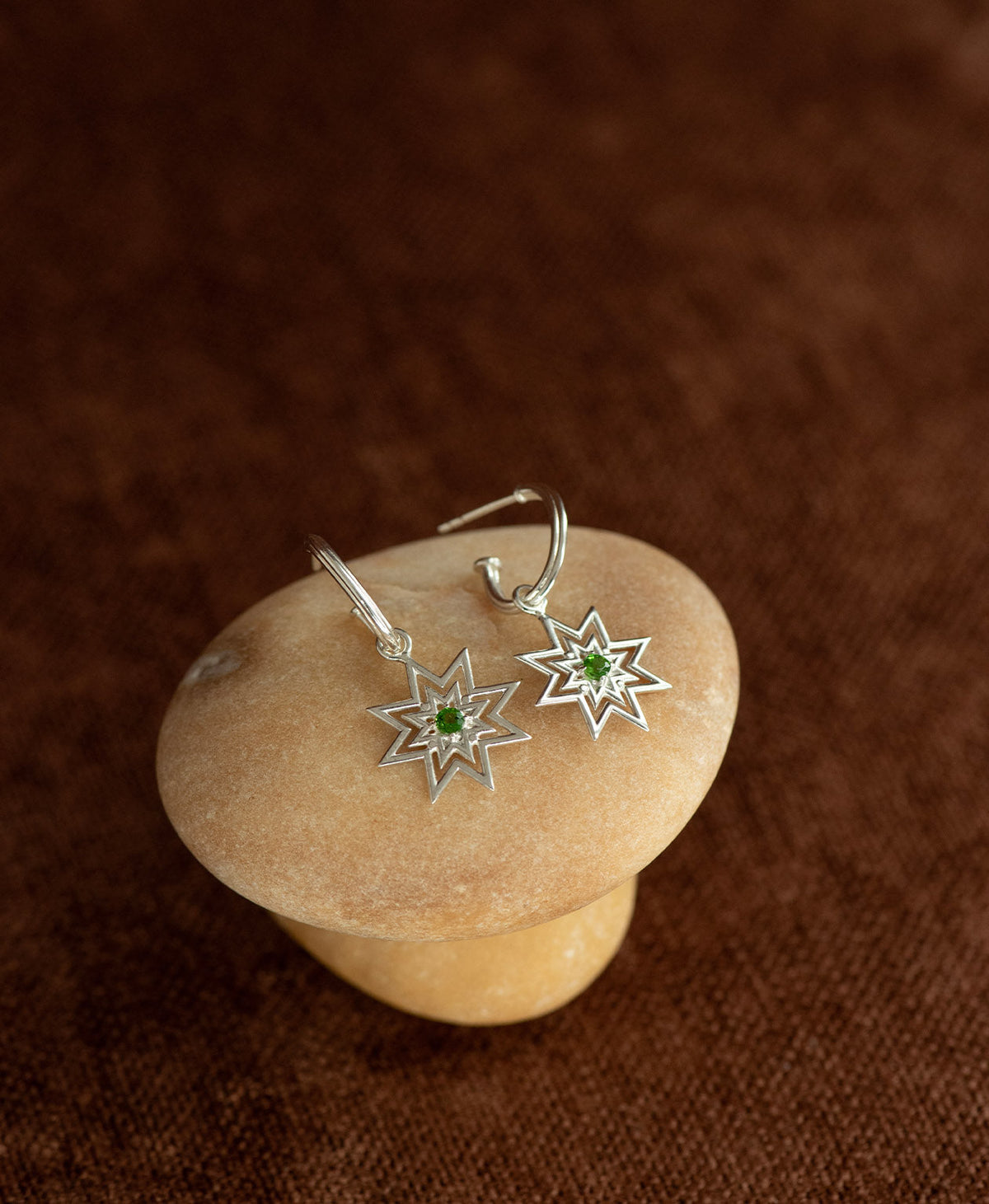 The Nora Hoops in 925 Sterling Silver with Chrome Diopside, resting on a stone.