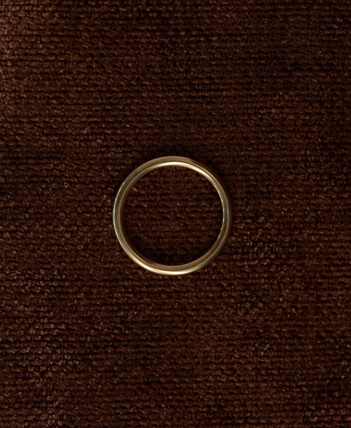 A close up of the smooth, curved Selma stacking ring in 22k gold vermeil, resting on a textured brown background.