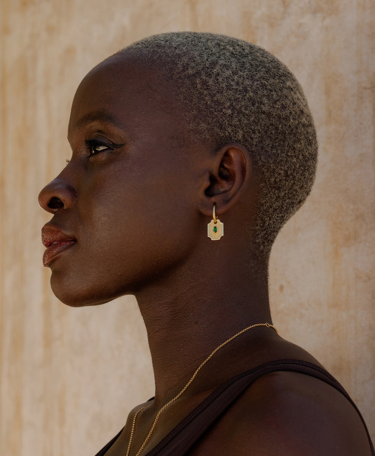 A close-up of a person wearing the Soul Sister Hoops, featuring a textured gold pendant with a central green stone on a hoop.