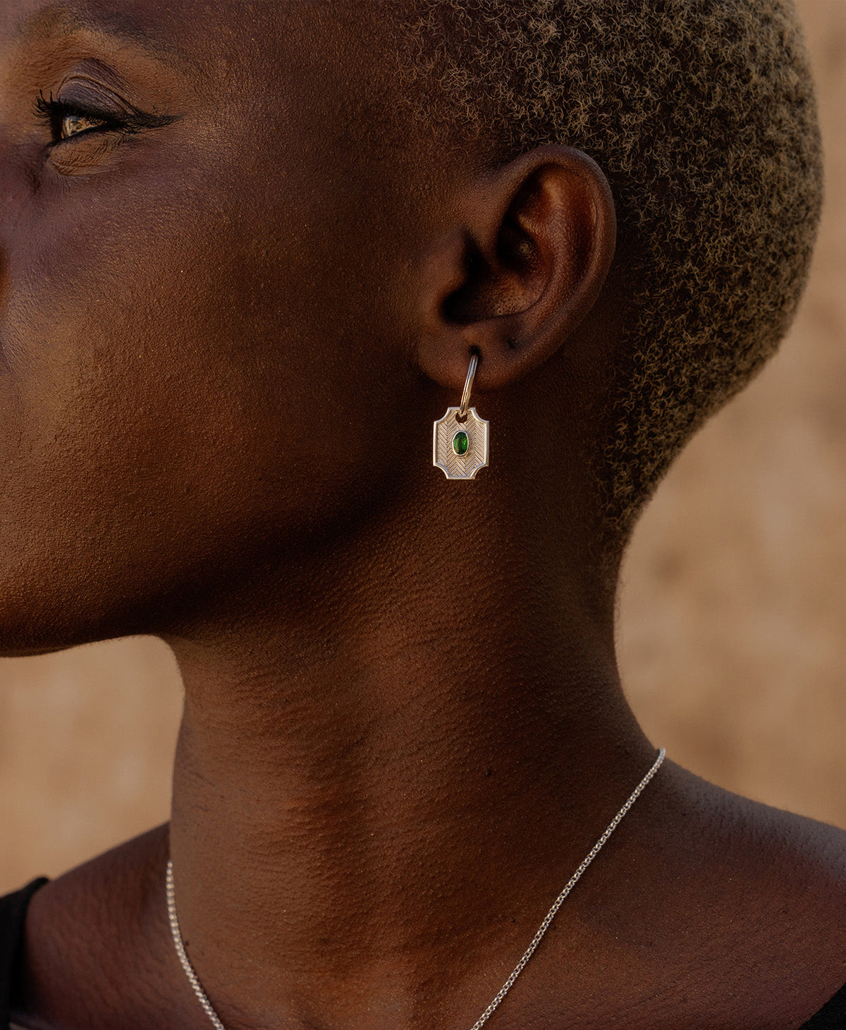 A close-up side profile of a person wearing the Soul Sister Hoops, featuring a textured silver pendant with a central green stone on a hoop.