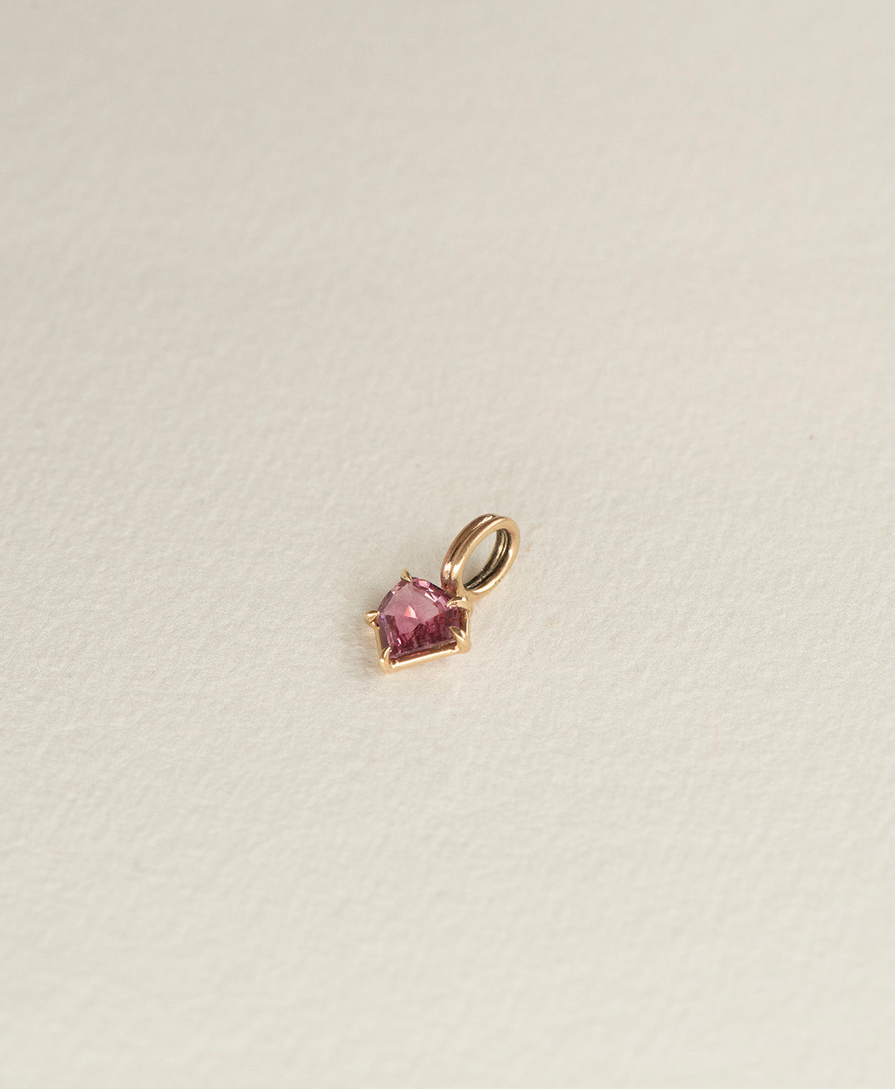 Angled view of the One of a Kind Charm 494 in 9k Yellow Gold with a vibrant fuchsia pink portrait cut Sapphire.