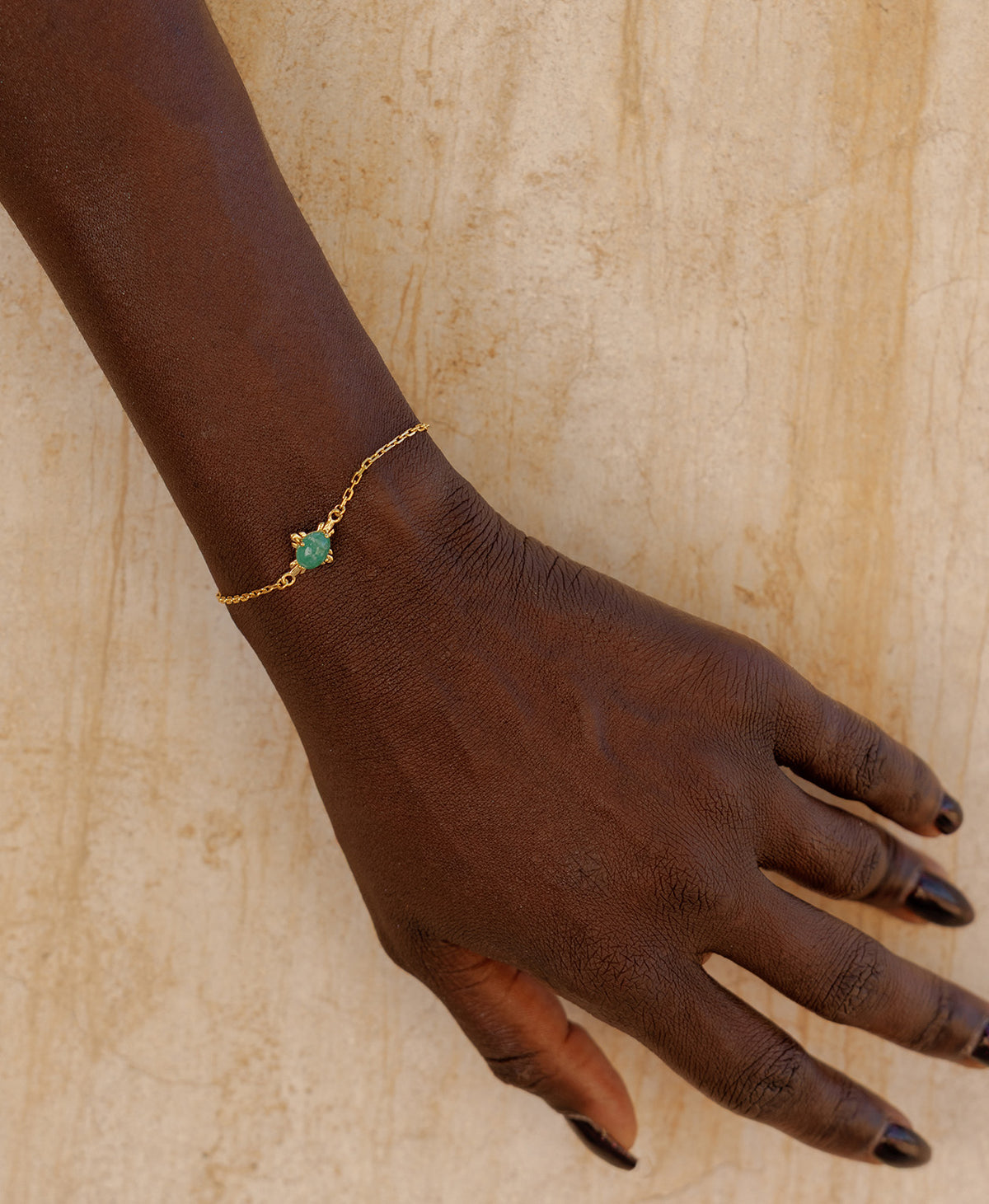 A close-up of an arm wearing the Farah Bracelet, a gold pendant with a cabochon cut emerald, set on a fine cable chain.