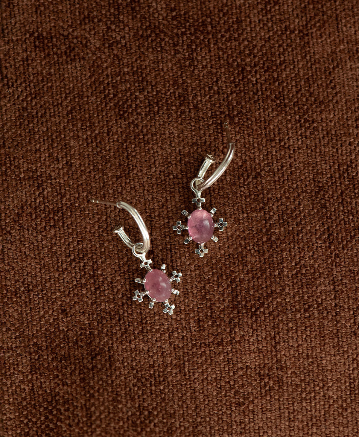 A pair of Farah silver drop earrings with pink tourmaline gemstones, displayed on a textured brown fabric background.