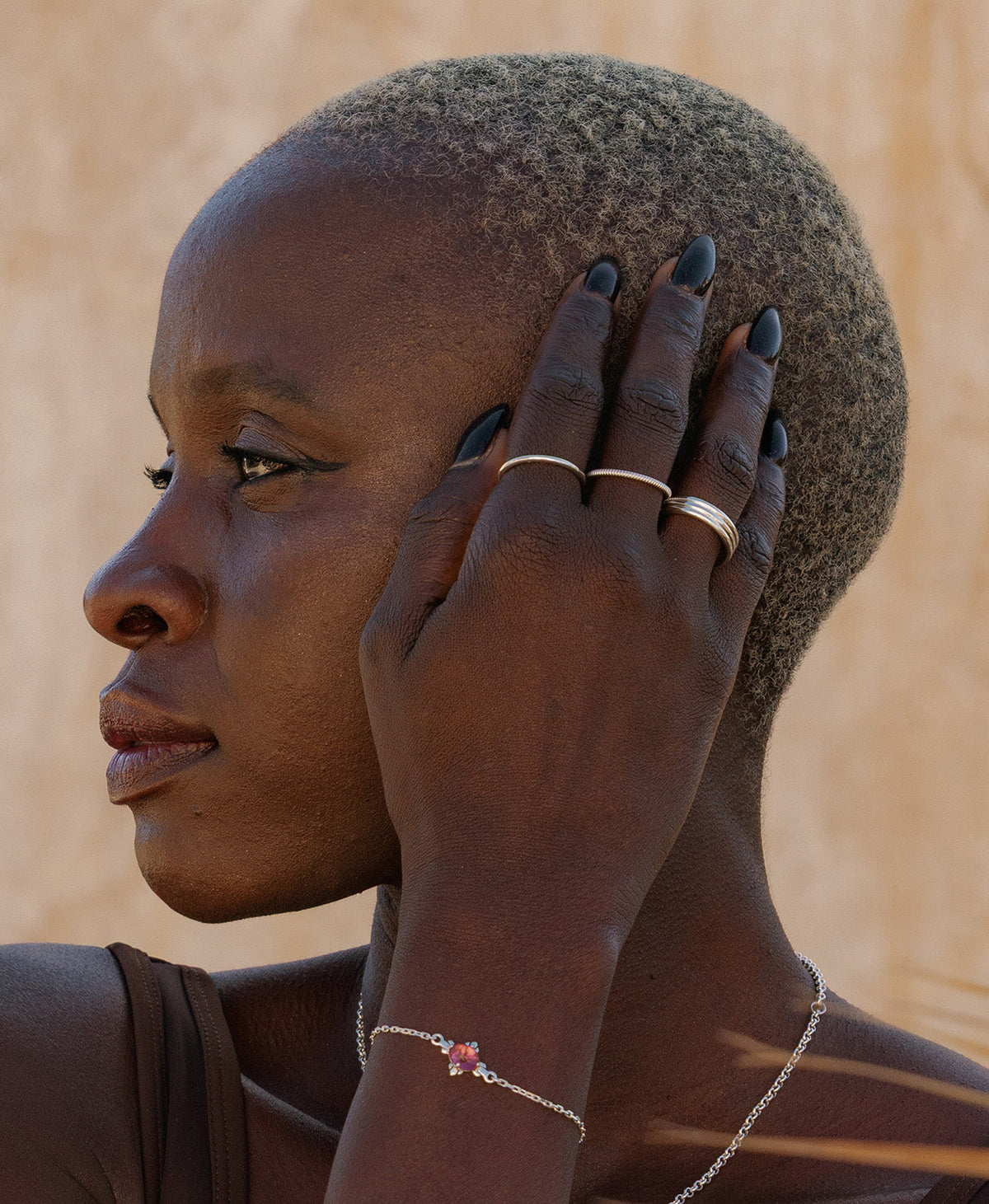 A closeup of a person wearing the Irma Stacking Ring on their ring finger, a thick silver band, paired with two thin stacking rings and a bracelet with a pink tourmaline. 