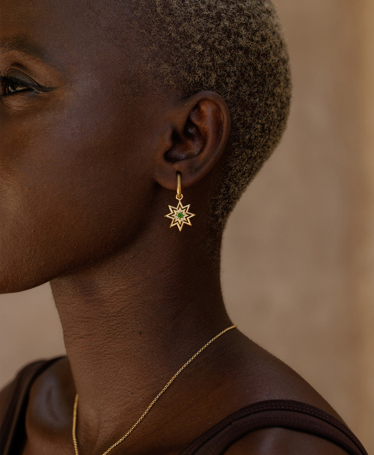 A close-up side profile of a person wearing the Nora Hoops, featuring a gold star hanging from a hoop with a central green stone.