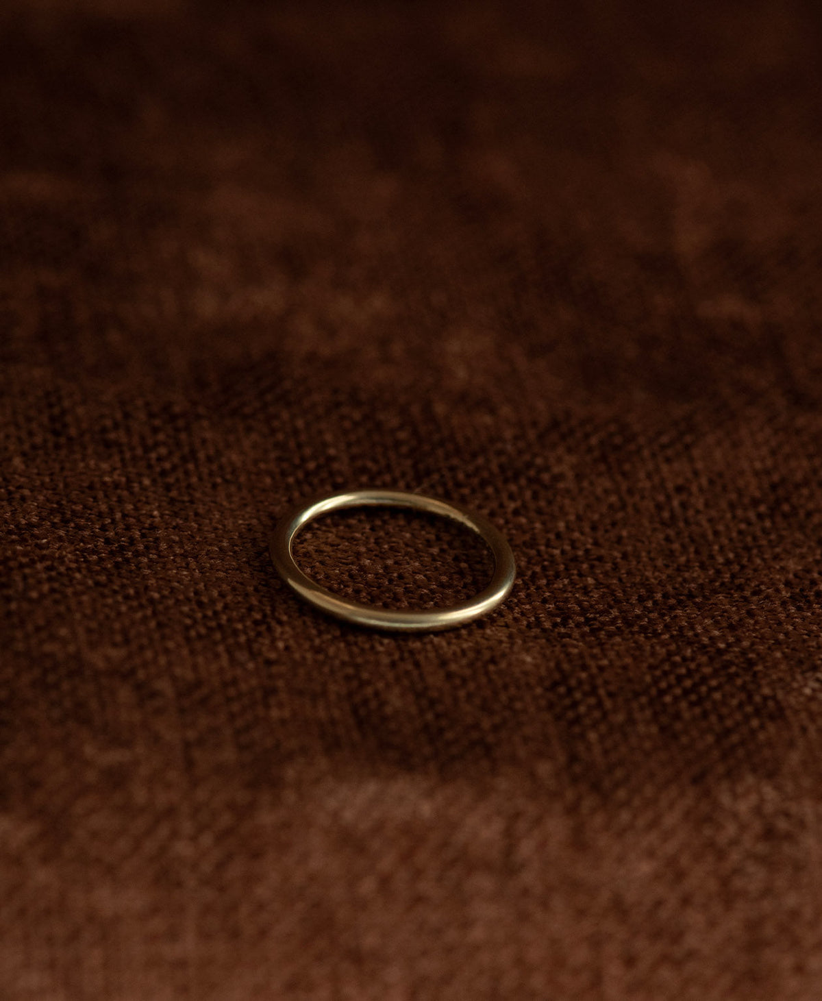 The smooth, curved Selma stacking ring in 22k gold vermeil, rests on a textured brown background. 