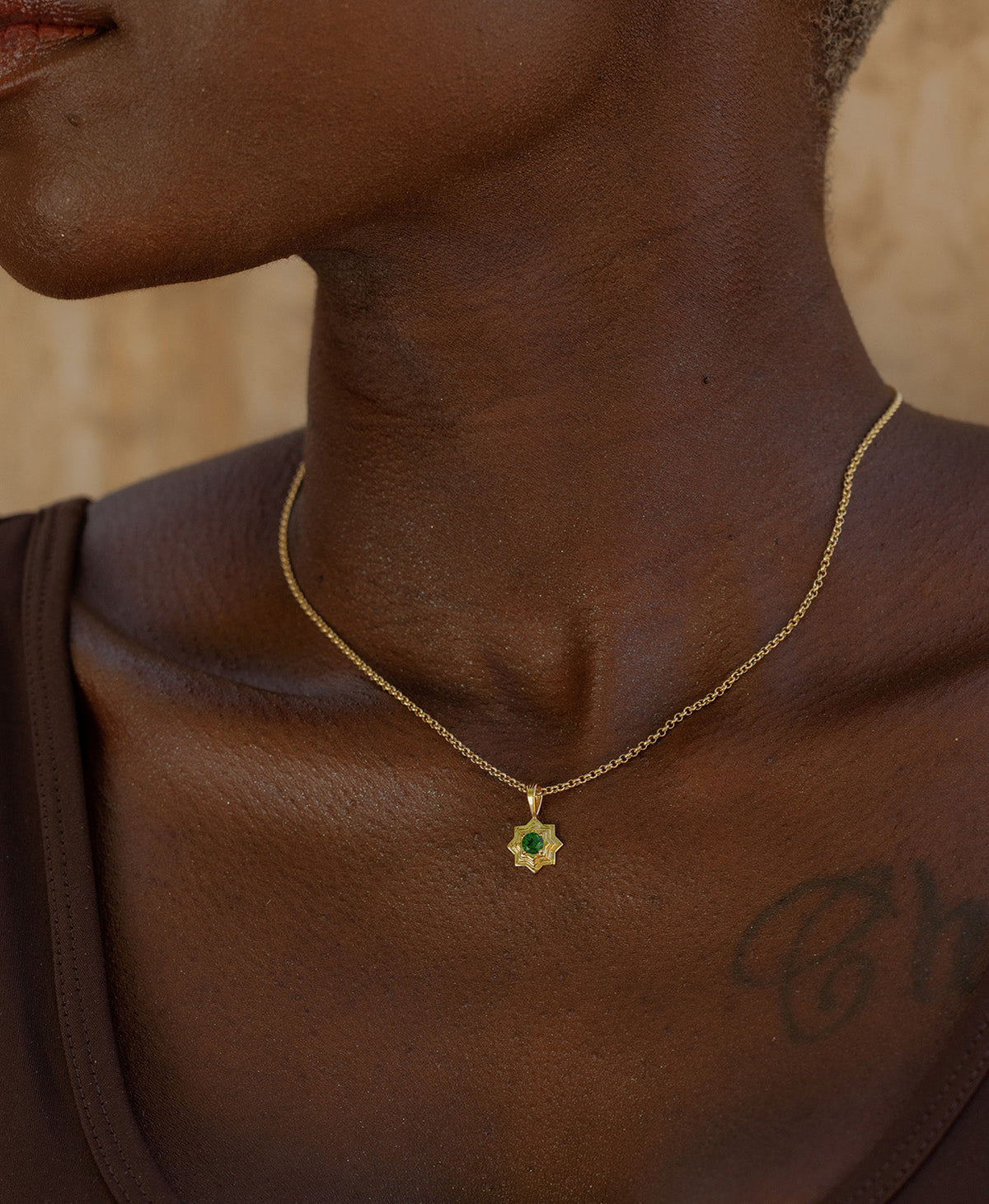A close-up of a neck wearing the Sitara Necklace, a gold star-like pendant with a central green stone. 